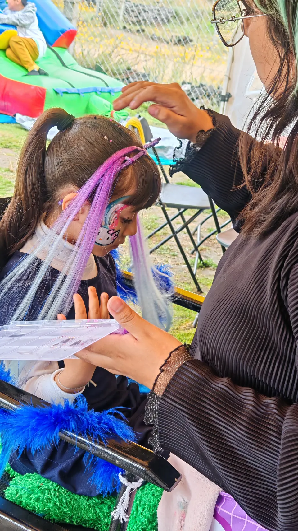 Niña con extensiones de colores en el cabello mientras le pintan la cara