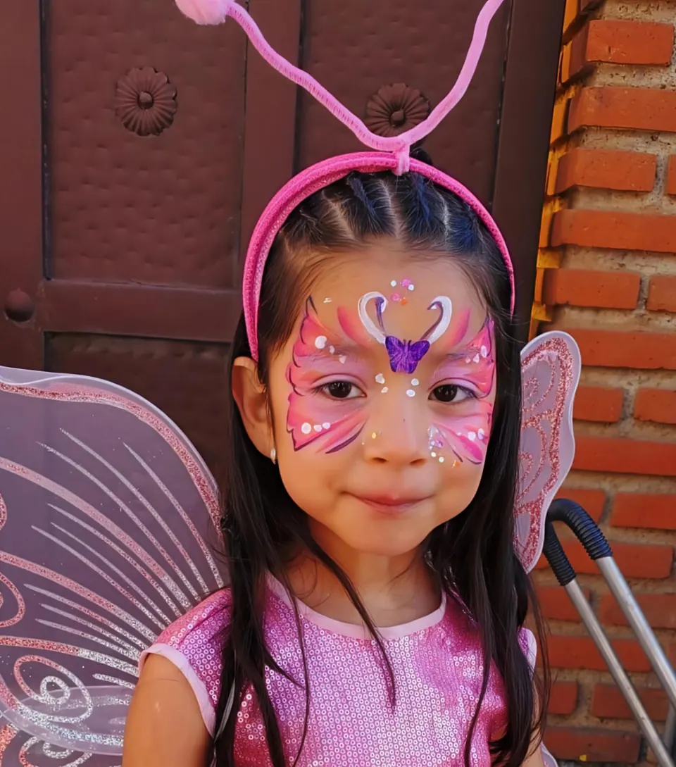 Niña con mariposa rosa pintada en la cara y alas de hada