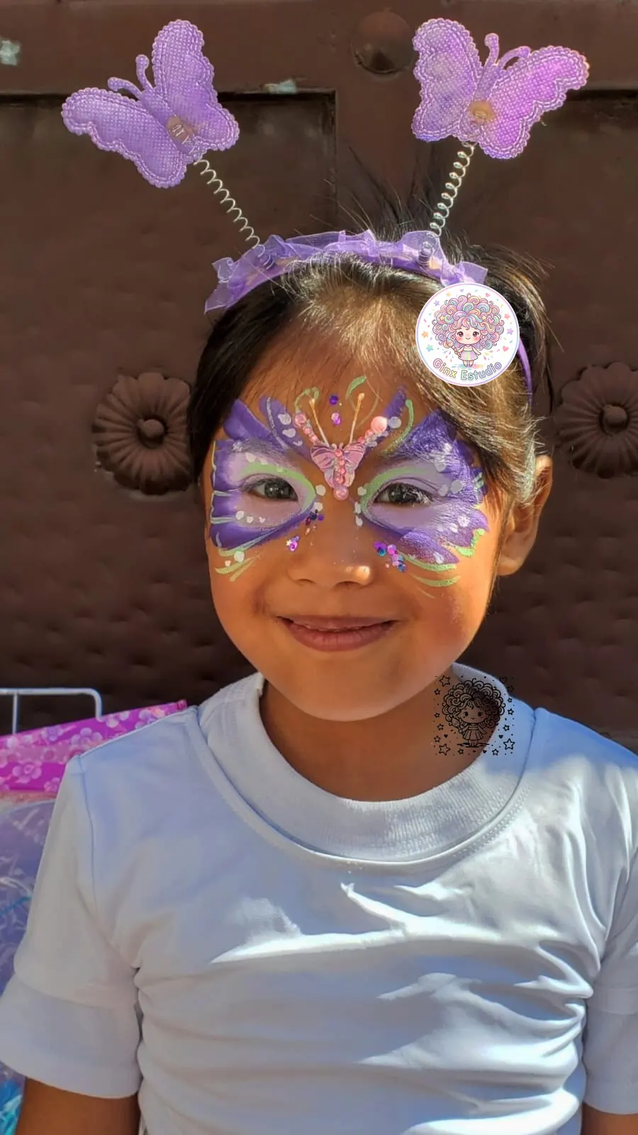 Niña sonriente con mariposa lila pintada y diadema de mariposas